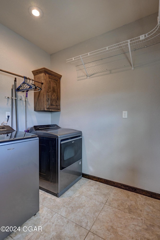 laundry area featuring light tile patterned floors, washing machine and clothes dryer, and cabinets