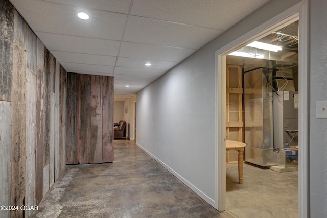 corridor with wooden walls, concrete flooring, and a paneled ceiling