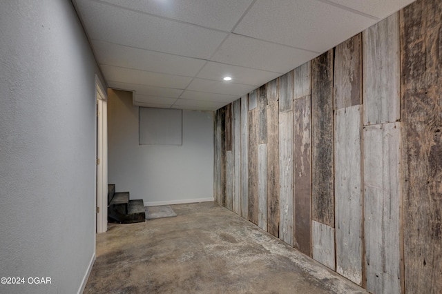 basement featuring a drop ceiling and wooden walls