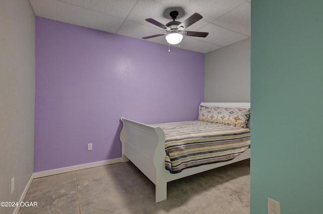 bedroom with a drop ceiling, ceiling fan, and concrete flooring