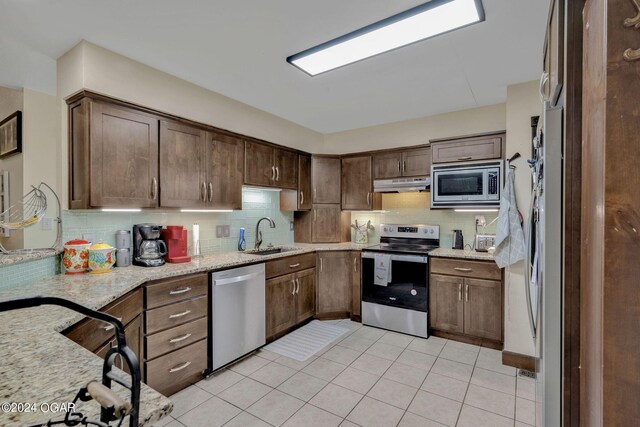 kitchen featuring light tile patterned floors, sink, backsplash, appliances with stainless steel finishes, and light stone countertops