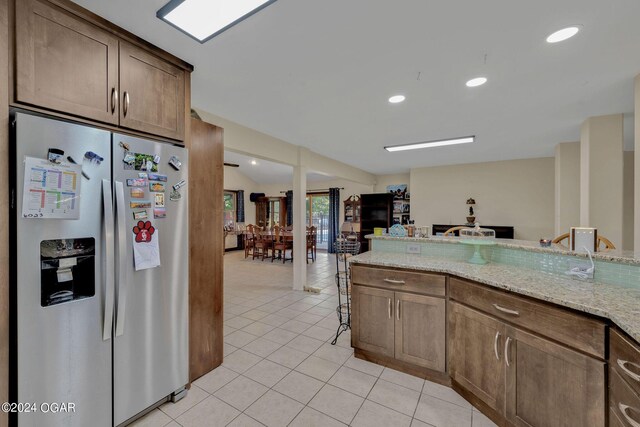 kitchen featuring light tile patterned floors, lofted ceiling, stainless steel fridge with ice dispenser, and light stone counters