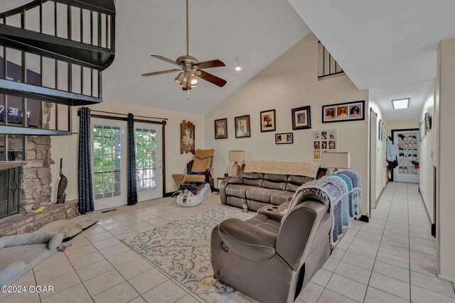 tiled living room with a stone fireplace, ceiling fan, and high vaulted ceiling