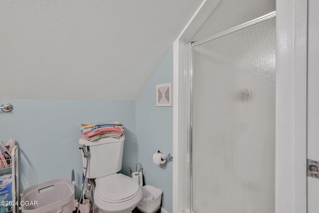 bathroom featuring lofted ceiling, a shower with door, and toilet