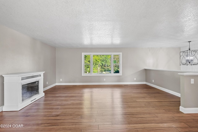 unfurnished living room featuring a textured ceiling, dark hardwood / wood-style floors, and a chandelier