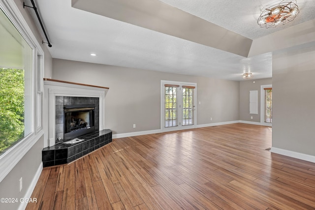 unfurnished living room with light hardwood / wood-style flooring, a tiled fireplace, and a textured ceiling