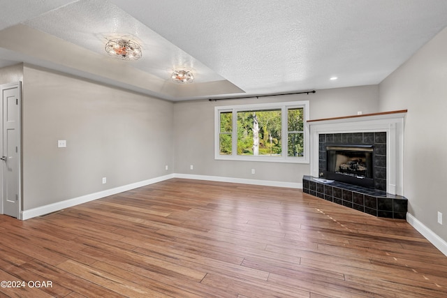 unfurnished living room with wood-type flooring, a textured ceiling, and a tile fireplace