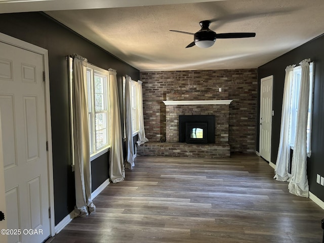 unfurnished living room with ceiling fan, dark wood-type flooring, a textured ceiling, and a brick fireplace