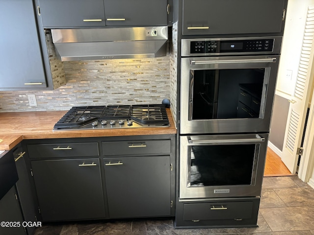 kitchen featuring appliances with stainless steel finishes, backsplash, ventilation hood, gray cabinets, and butcher block countertops