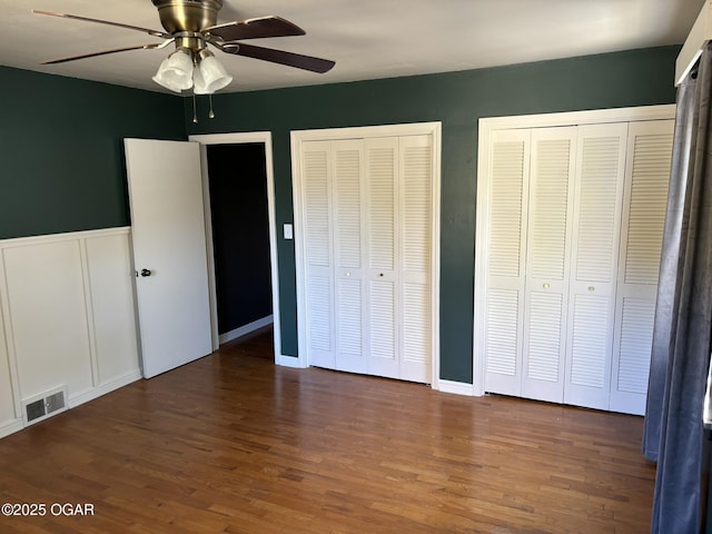 unfurnished bedroom with ceiling fan, dark hardwood / wood-style flooring, and two closets