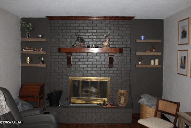 living room featuring a textured ceiling, built in shelves, hardwood / wood-style floors, and a brick fireplace