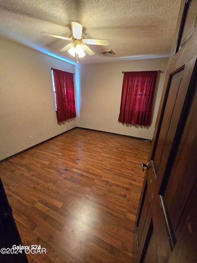 empty room with ceiling fan, a textured ceiling, and dark wood-type flooring