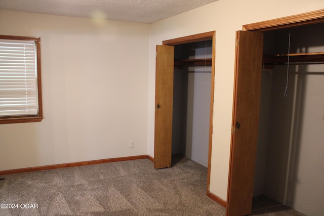 unfurnished bedroom featuring two closets, carpet, and a textured ceiling