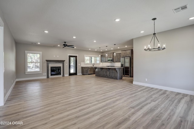 unfurnished living room with light hardwood / wood-style floors, a textured ceiling, and ceiling fan with notable chandelier