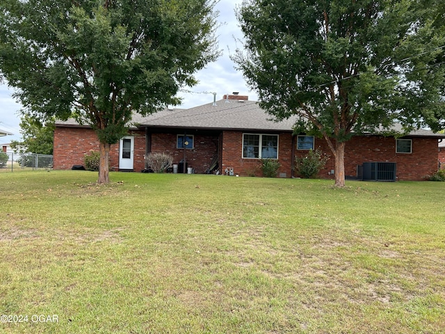 rear view of house featuring central AC unit and a lawn