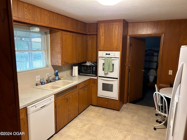 kitchen with white appliances, wooden walls, sink, and backsplash