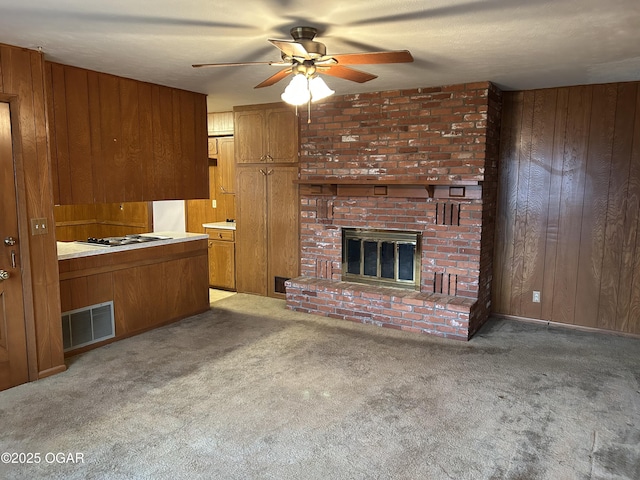 unfurnished living room featuring light carpet, a brick fireplace, ceiling fan, and wood walls