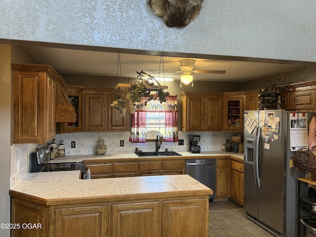 kitchen with a peninsula, a sink, light countertops, appliances with stainless steel finishes, and glass insert cabinets