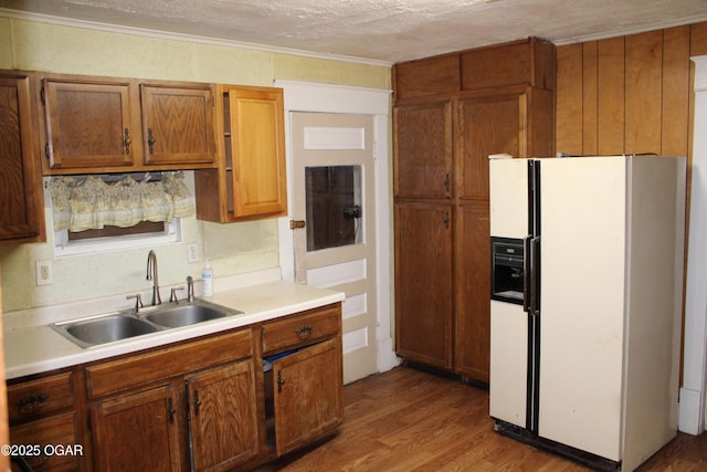 kitchen with sink, crown molding, wood-type flooring, a textured ceiling, and white fridge with ice dispenser