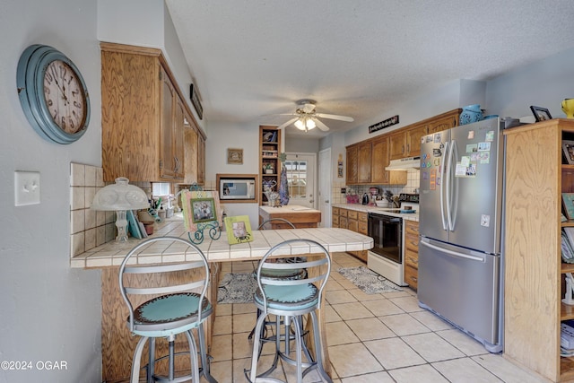 kitchen with tile counters, kitchen peninsula, a kitchen bar, stainless steel fridge, and white electric range