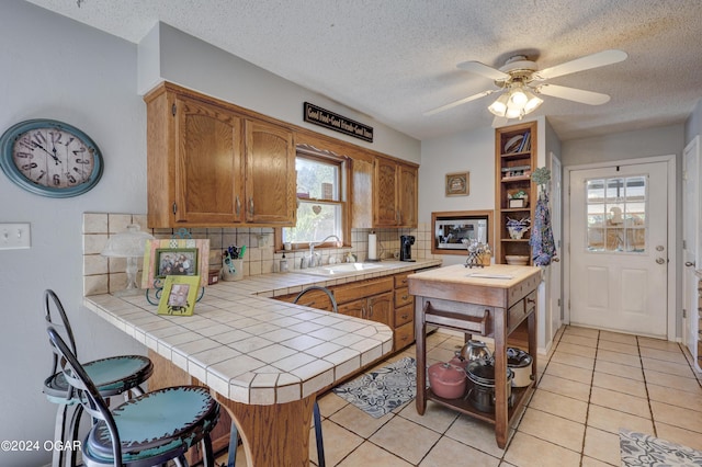 kitchen with decorative backsplash, light tile patterned flooring, kitchen peninsula, tile countertops, and sink