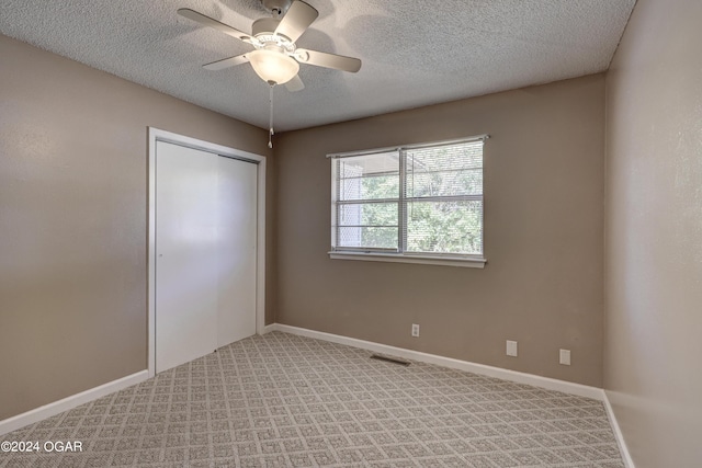 unfurnished bedroom featuring a closet, a textured ceiling, light colored carpet, and ceiling fan