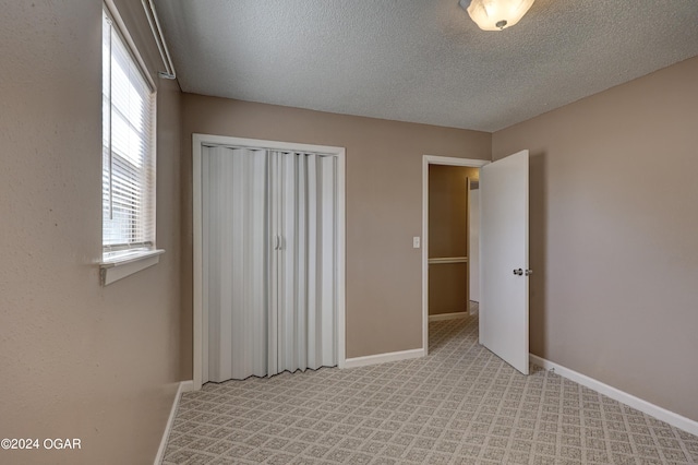 unfurnished bedroom featuring a closet, a textured ceiling, and light colored carpet