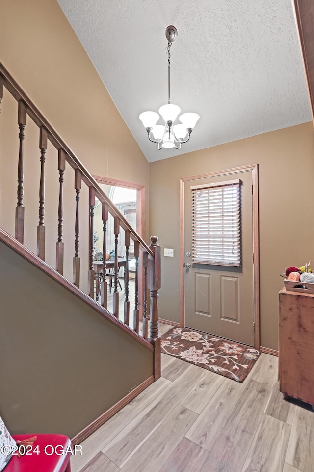 foyer entrance with vaulted ceiling, an inviting chandelier, light wood-type flooring, and a textured ceiling