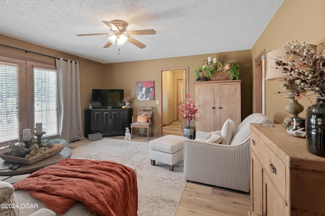 living room with a textured ceiling, ceiling fan, and light hardwood / wood-style flooring