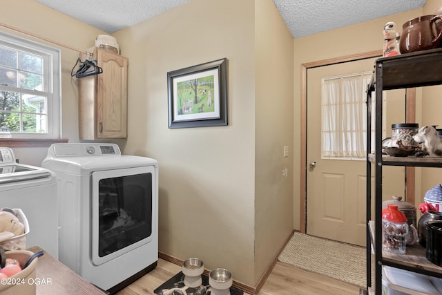 clothes washing area featuring washing machine and dryer, light hardwood / wood-style floors, cabinets, and a textured ceiling