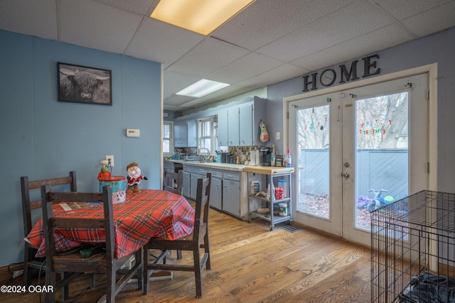 dining area with sink, french doors, a drop ceiling, and light wood-type flooring