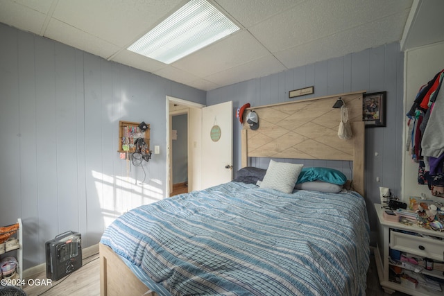 bedroom featuring wood walls, hardwood / wood-style floors, and a drop ceiling