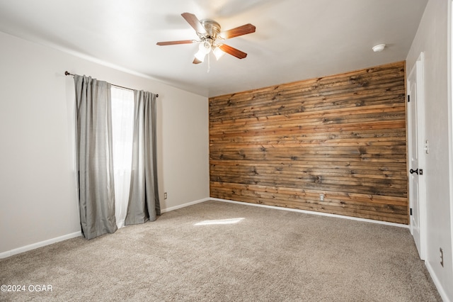 carpeted empty room with ceiling fan and wood walls