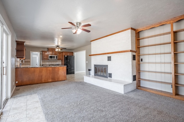 unfurnished living room featuring light carpet, sink, a brick fireplace, a textured ceiling, and ceiling fan