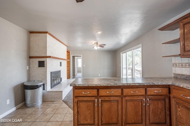 kitchen with ceiling fan, kitchen peninsula, light tile patterned flooring, and a brick fireplace