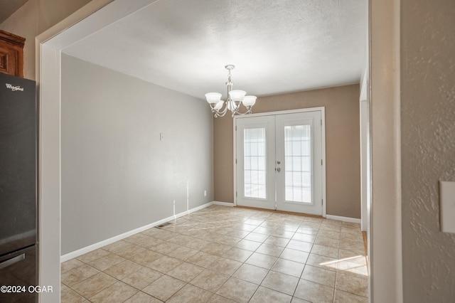 tiled spare room with a chandelier, a textured ceiling, and french doors