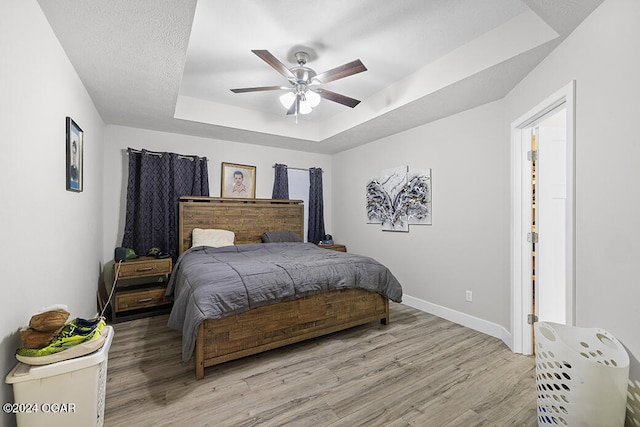 bedroom with a raised ceiling, a textured ceiling, light wood-type flooring, and ceiling fan