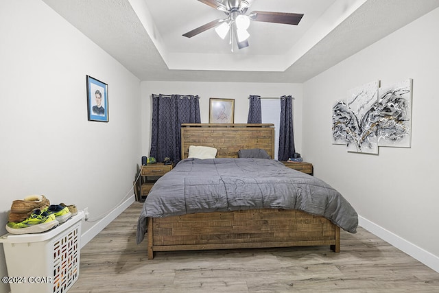 bedroom with a raised ceiling, light hardwood / wood-style floors, and ceiling fan