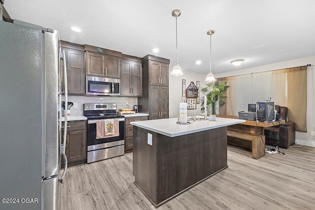 kitchen featuring appliances with stainless steel finishes, light hardwood / wood-style floors, dark brown cabinetry, decorative light fixtures, and a center island with sink