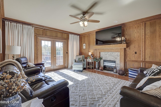 living room with wood walls, french doors, a tile fireplace, crown molding, and ceiling fan