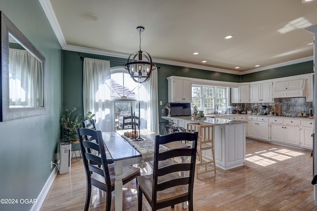 dining space featuring sink, a chandelier, light hardwood / wood-style flooring, and crown molding