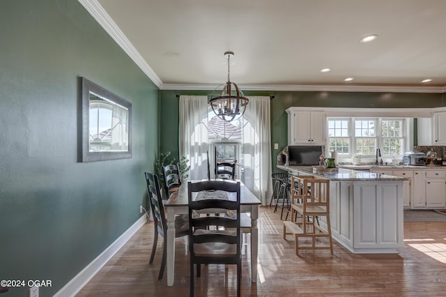 dining space with light wood-type flooring, crown molding, sink, and a chandelier