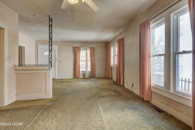 unfurnished living room featuring a textured ceiling, a healthy amount of sunlight, carpet flooring, and ceiling fan