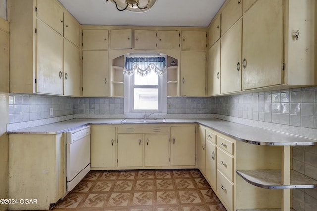 kitchen with white dishwasher, sink, cream cabinetry, and backsplash