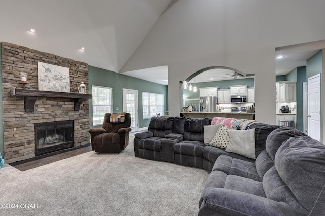 carpeted living room with a stone fireplace, high vaulted ceiling, and ceiling fan