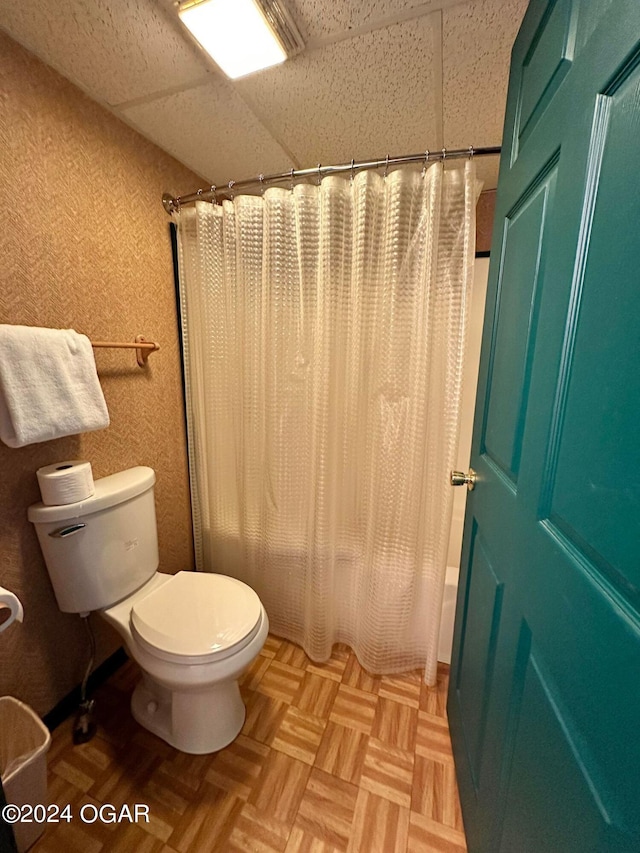 bathroom featuring toilet, a paneled ceiling, shower / bathtub combination with curtain, and parquet flooring