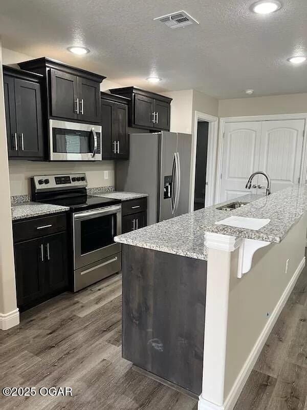 kitchen with appliances with stainless steel finishes, a textured ceiling, sink, a center island with sink, and dark hardwood / wood-style floors