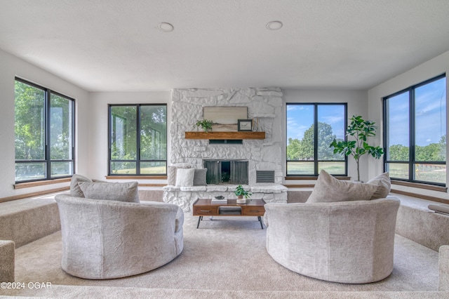 living room with carpet flooring, a stone fireplace, and a textured ceiling