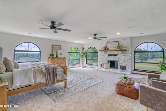 bedroom with a stone fireplace, a textured ceiling, light carpet, and multiple windows