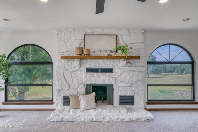 interior details with a stone fireplace, ceiling fan, carpet floors, and a textured ceiling